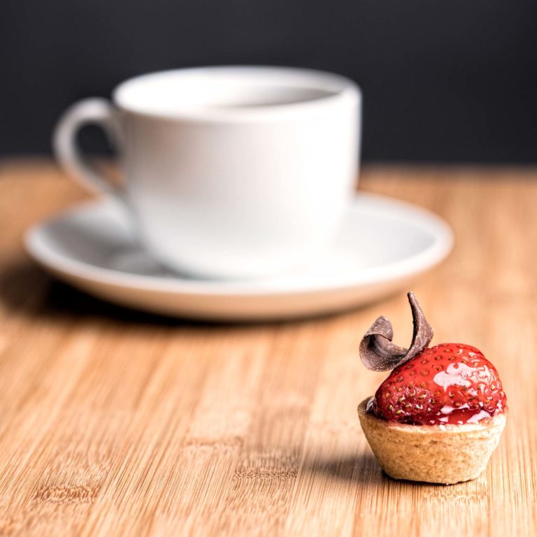 Strawberry tartlet with chocolate swirl and cup of tea