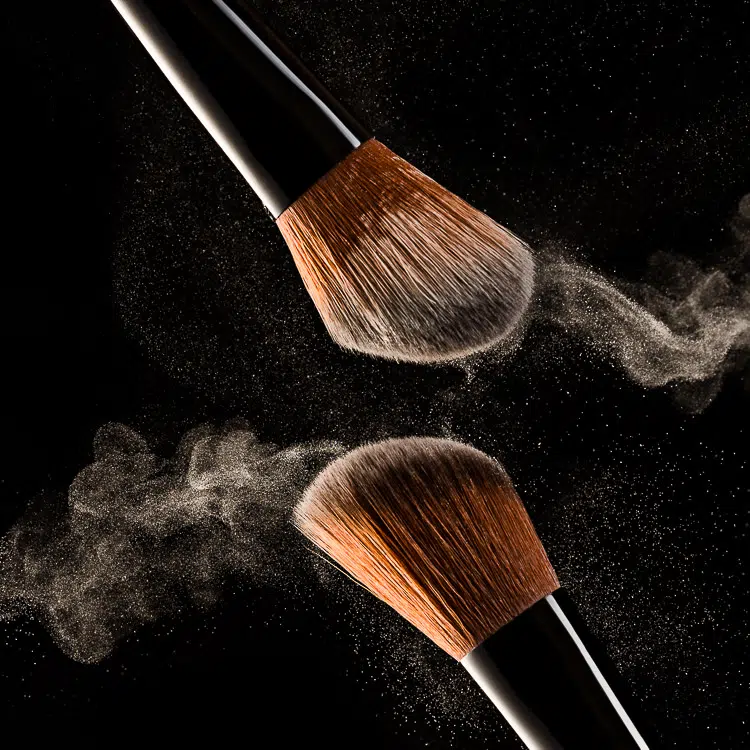Makeup brushes with face powder in the air on black background
